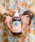 A 4 fl oz bottle of Glow Up Massage Oil with CBD by Appalachian Standard held by Lauren Davis of Fiddy Shades of Green