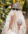 A ghost in a sheet with a cheetah bucket hat holding a bag of CBD ghoulish gummies in the greenhouse at Ross Farm Asheville, NC.