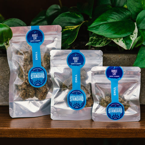 Appalachian Standard's Harle Cat Hemp Flower in three differently sized bags on a wooden shelf with plants in the background