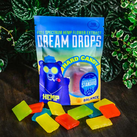 A bag of Appalachian Standard's Dream Drops CBD Hard Candy and 11 pieces of CBD hard candy with plants in background