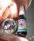 Appalachian Standard's Mountain Paradise CBD Body Oil with a pink satin sheet and shiny disco ball.