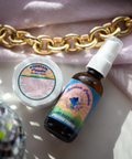 Appalachian Standard's Mountain Paradise CBD Body Oil and CBD Body Cream laying on a marble table with a disco ball and gold chain with a purple curtain.