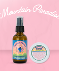 Appalachian Standard Mountain Paradise Body Oil in an amber bottle and body cream in a white container on a baby pink background