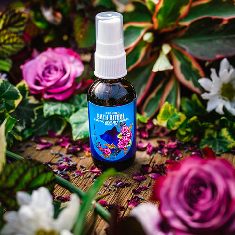 A 2 oz bottle of Appalachian Standard's For the Love of Flowers Body Oil with CBD on a wooden table surrounded by roses and lavender