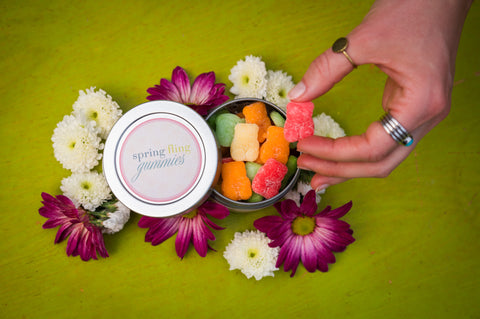 Hand reaching for a container of gummy bears surrounded by flowers on a green background