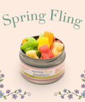 Appalachian Standard Spring Fling Gummies tin, open and overflowing with colorful sugar-coated gummies in green, yellow, red, and orange on a soft peach background with illustrated floral vine accents. Flavors include Coconut Lime, Lemon Meringue Pie, Strawberry Pound Cake, Mango Ice Cream, and Orange Creamsicle.