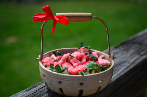 Close-up of handcrafted berry basket containing fresh strawberries and Appalachian Standard strawberry hemp gummies with red bow on weathered wood, CBD products from Asheville NC
