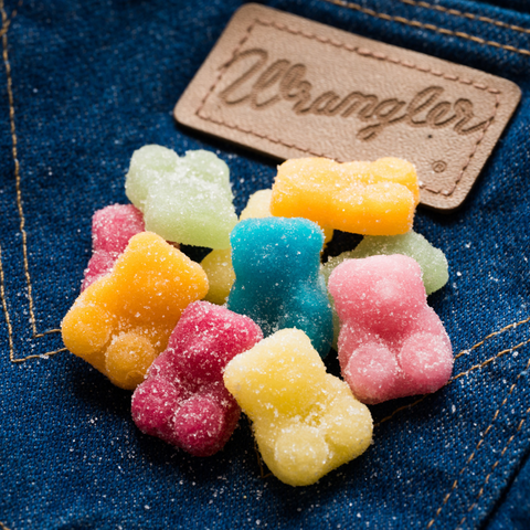 Colorful Sugar Daddies gummy bears scattered on denim with Wranglers leather patch - altitude adjusting gummies