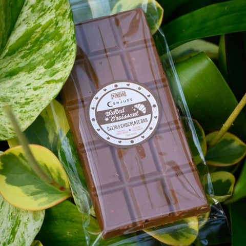 Appalachian Standard's Salted Croissant THC Chocolate bar in cellophane wrapping surrounded by plant leafs.