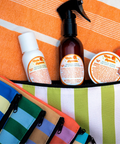 Appalachian Standard Tropical Citrus Main Squeeze CBD skincare trio — body lotion, after-sun mist spray, and body cream — displayed in one of the 6 colorful striped travel pouches they come with, on an orange beach towel.