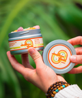 Hands holding an open tin of Appalachian Standard Acapulco Gold Gummies with the lid displayed separately, showing 30 full-spectrum CBD gummies in assorted flavors, with a hemp plant in the background