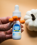Hand holding a small bottle with a dropper next to a white pumpkin on a beige background