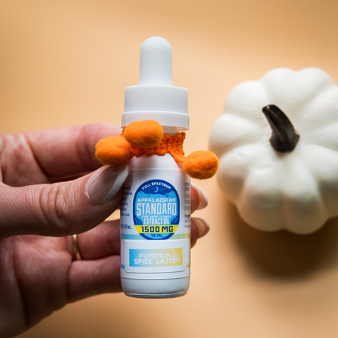 Hand holding a small bottle with a dropper next to a white pumpkin on a beige background