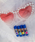 Pink pearl heart-shaped sunglasses with rose-tinted lenses next to four CBD vape cartridges on romantic white lace background