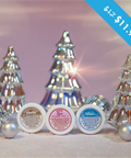 A photo of Appalachian Standards Holly Jolly Hydration Set, featuring their Limited Edition body creams, sandalwood vanilla, snow kiss, and Appalachian winter. The photo has the body creams surrounded by shiny glass tree decorations, disco balls and ornaments.