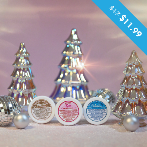 A photo of Appalachian Standards Holly Jolly Hydration Set, featuring their Limited Edition body creams, sandalwood vanilla, snow kiss, and Appalachian winter. The photo has the body creams surrounded by shiny glass tree decorations, disco balls and ornaments.