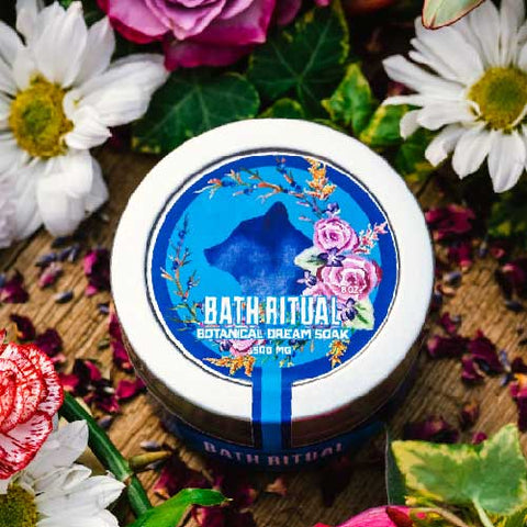 An overhead view of Appalachian Standard's tin of CBD Botanical Dream Bath Soak on a piece of wood surrounded by flowers and plants