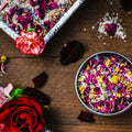 An 8 oz tin filled with bath salts, rose petals, chamomile flowers, and lavender from Appalachian Standard's CBD Botanical Dream Bath Soak on a piece of wood surrounded by flowers