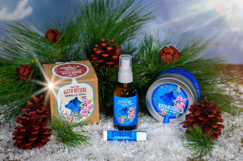 A box of Appalachian Standard's CBD Bath Bomb, a bottle of Appalachian Standard's For the Love of Flowers CBD Body Oil, a tin of Appalachian Standard's CBD Body Polish, and a tube of Appalachian Standard's CBD Chapstick surrounded by pine needles and pine cones