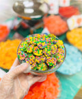 Hand holding a small container of colorful candies with a blurred candy display in the background. These are Bouj Bite Clusters from Appalachian Standard.