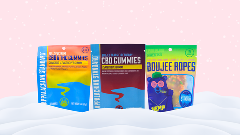 Three colorful product packages on a white surface with a pink gradient background