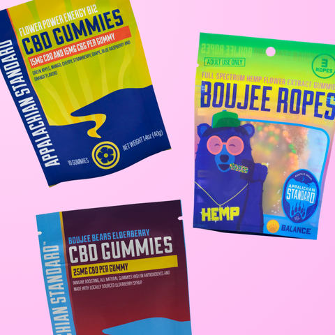 Three Appalachian Standard products on a pink background: Flower Power Energy B12 CBD Gummies bag (15mg CBD and 15mg CBG per gummy), Boujee Ropes full spectrum hemp flower extract gummies bag with a cartoon bear illustration, and Boujee Bears Elderberry CBD Gummies bag (25mg CBD per gummy)