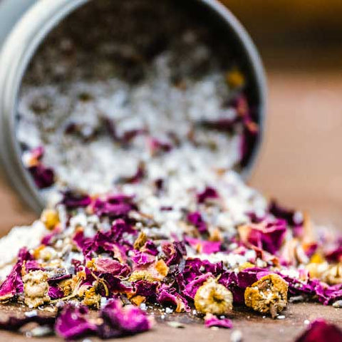 Rose petals, bath salts, chamomile flowers, and lavender spilled out of an 8 oz tin of Appalachian Standard's CBD Botanical Dream Bath Soak