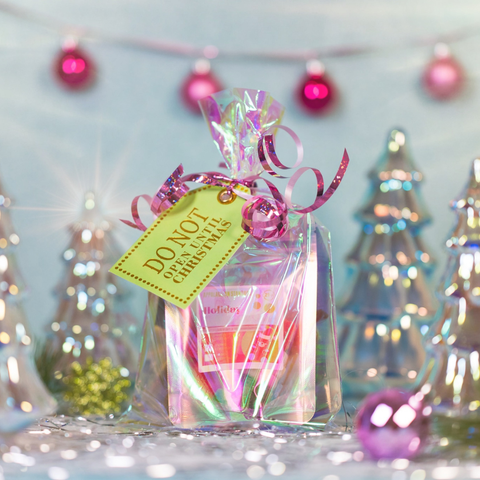 Gift bag with a tag and ribbons against a festive background with Christmas trees and lights.