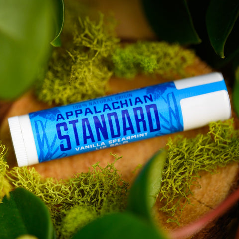 A stick of Appalachian Standard's Vanilla Spearmint CBD Lip Balm on a piece of wood surrounded by plants