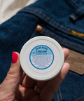 Appalachian Standard Dad Bod Cream, 1.5 oz jar, with 188mg CBD, being held by a hand over a pair of Wrangler jeans.