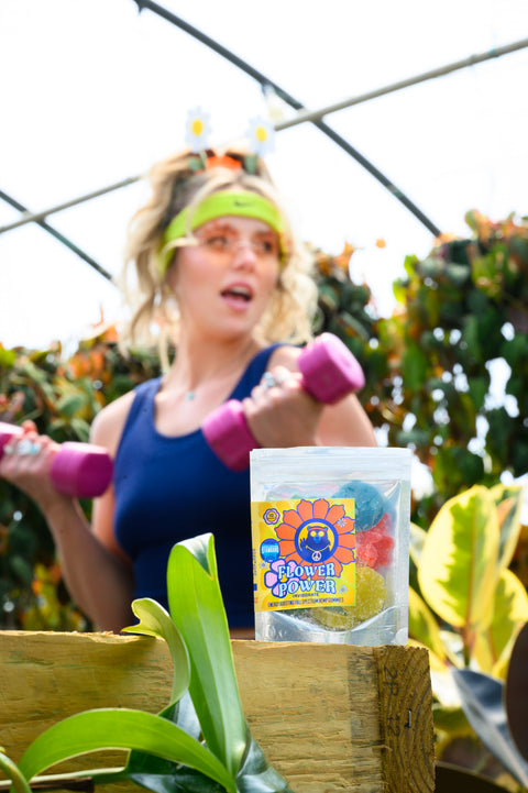 Woman exercising with dumbbells in a greenhouse setting, with a Power Bar product in the foreground.