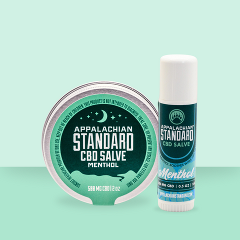 Two containers of Appalachian Standard CBD Salve, one as a tin container and the other as a stick, both labeled with 'Menthol' and containing 500 mg CBD each.