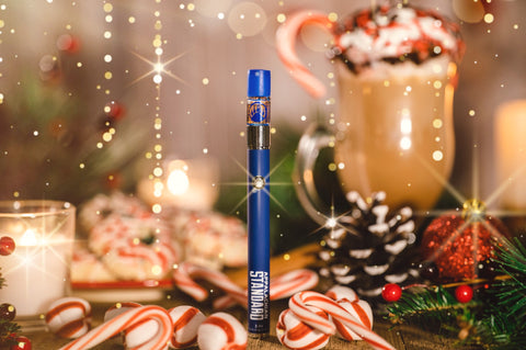 Appalachian Standard's Peppermint Mocha CBD Vape standing upright on a wooden table surrounded by candy canes and a pine cone with a glass of hot chocolate in the background