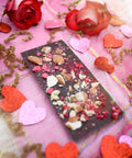 A bar of Appalachian Standard's Raspberry Almond CBD Dark Chocolate with crushed raspberries and almond pieces on top in a Valentine's Day setting