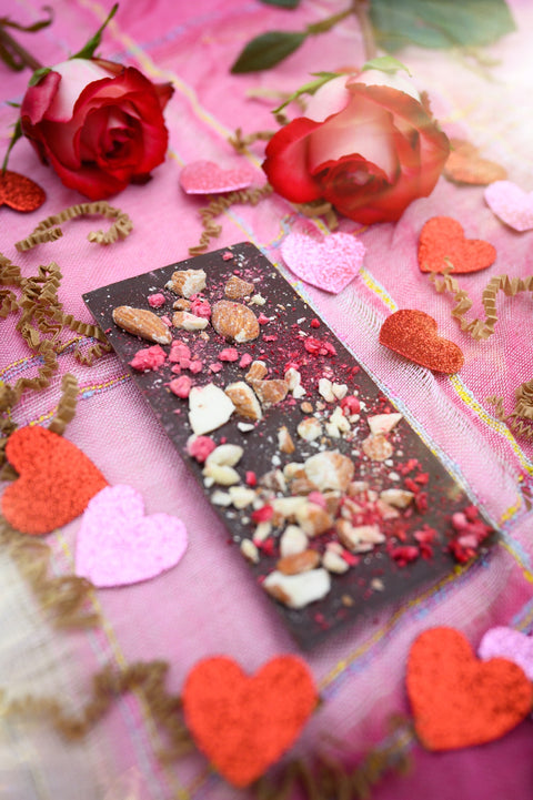 A bar of Appalachian Standard's Raspberry Almond CBD Dark Chocolate with crushed raspberries and almond pieces on top in a Valentine's Day setting