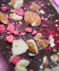 A bar of Appalachian Standard's Raspberry Almond CBD Dark Chocolate with crushed raspberries and almond pieces on top in a Valentine's Day setting