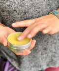 One hand holding a 2 oz tin of Appalachian Standard's Menthol CBD Salve while one finger from the other hand dips into the salve