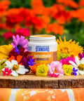 Appalachian Standard Soothe Operator CBD Muscle Gel container, with the lid off, displayed on natural wood round with an artistic arrangement of colorful garden flowers - yellow marigolds, purple asters, white cosmos, pink carnations, and red blooms.