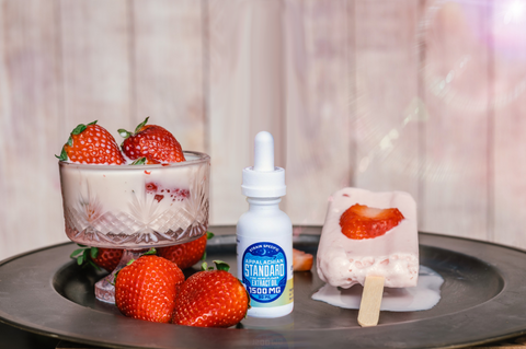 A bottle of Appalachian Standard's Strawberry Dreamsicle CBD Tincture on a plate with strawberries and a strawberry dreamsicle ice pop